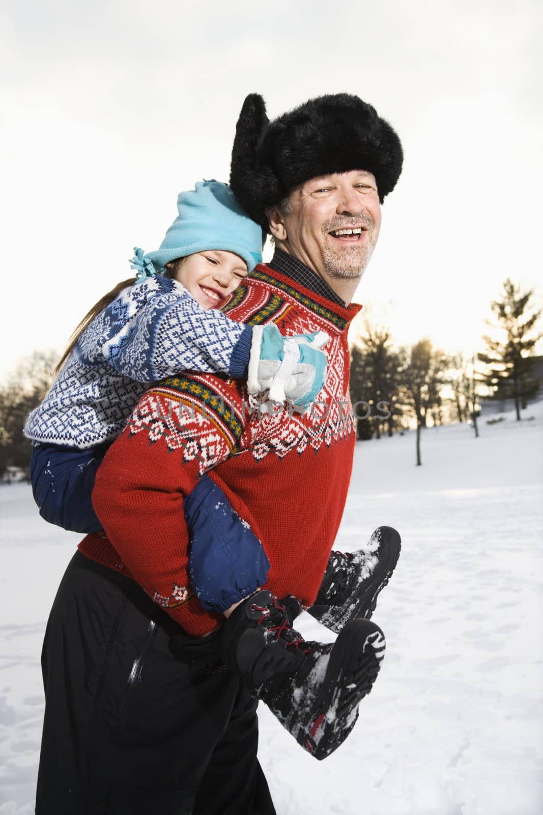Caucasian middle aged man holding Caucasian litte girl piggyback style smiling and looking at viewer smiling.