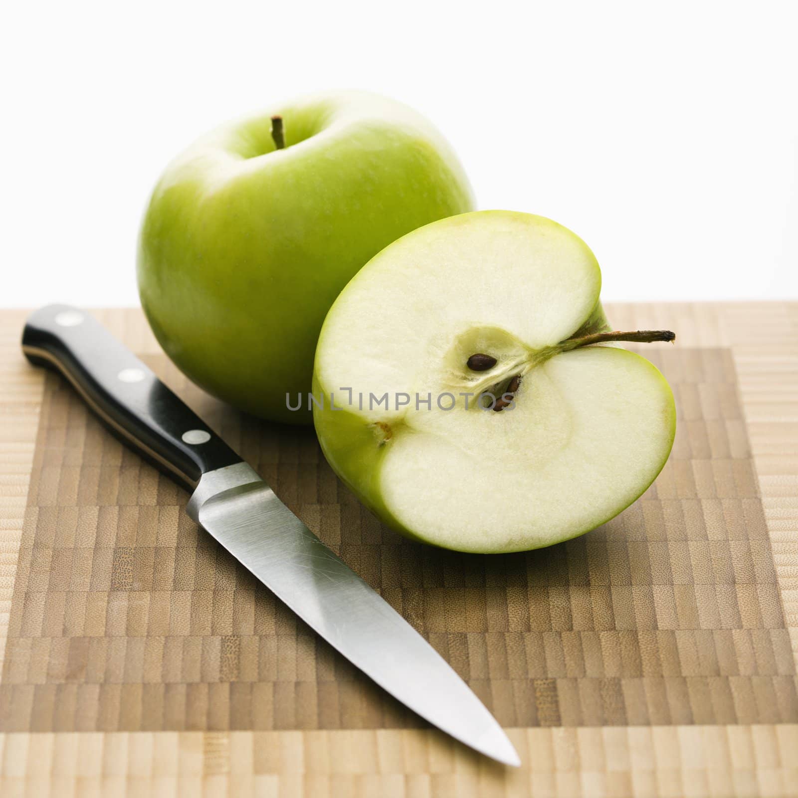 Still life of green apples and knife on cutting board.