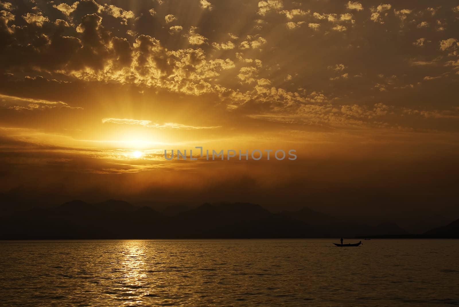 sunset on the sea side with silhouettes of mountans and fishermen.