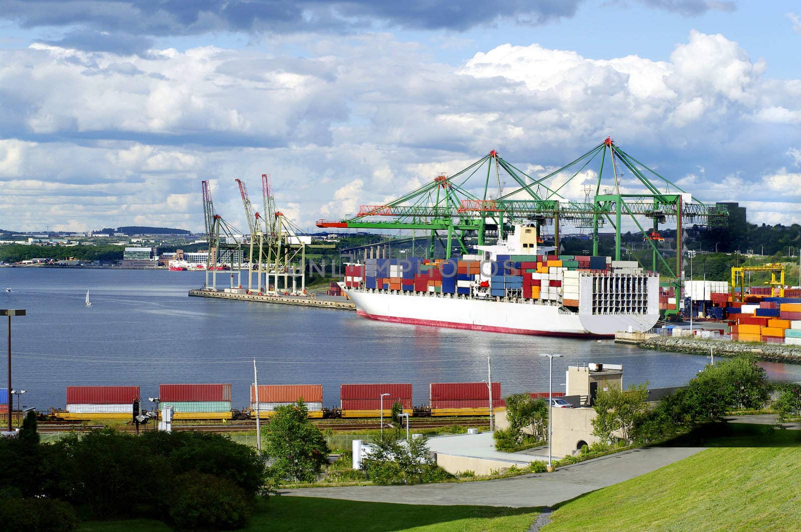 cargo ship at the waterfront with crane, storage, crates, railroad track and cargo train in foreground