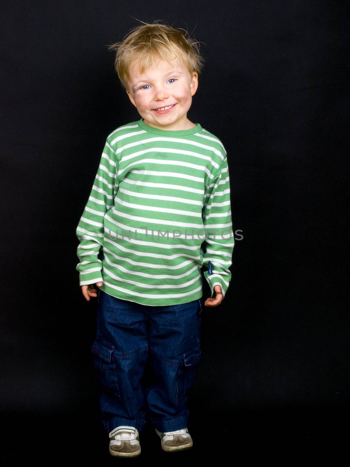 Smiling little boy on black background. Boy have blue eyes, blond hair and a bit of dirt on his face