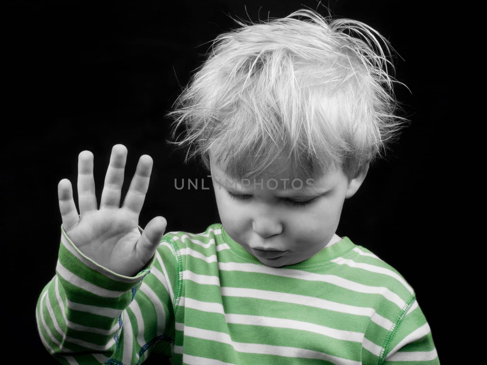 Litlle boy looking down and showing hand on black background, monochrome picture with only color green