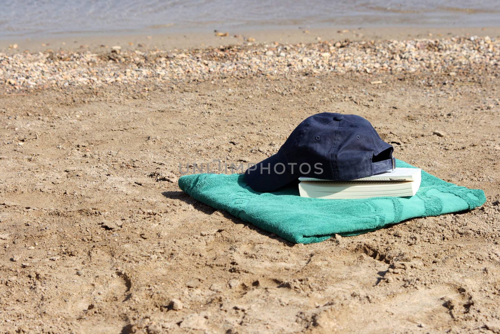 blue baseball hat on green towel by the see and book