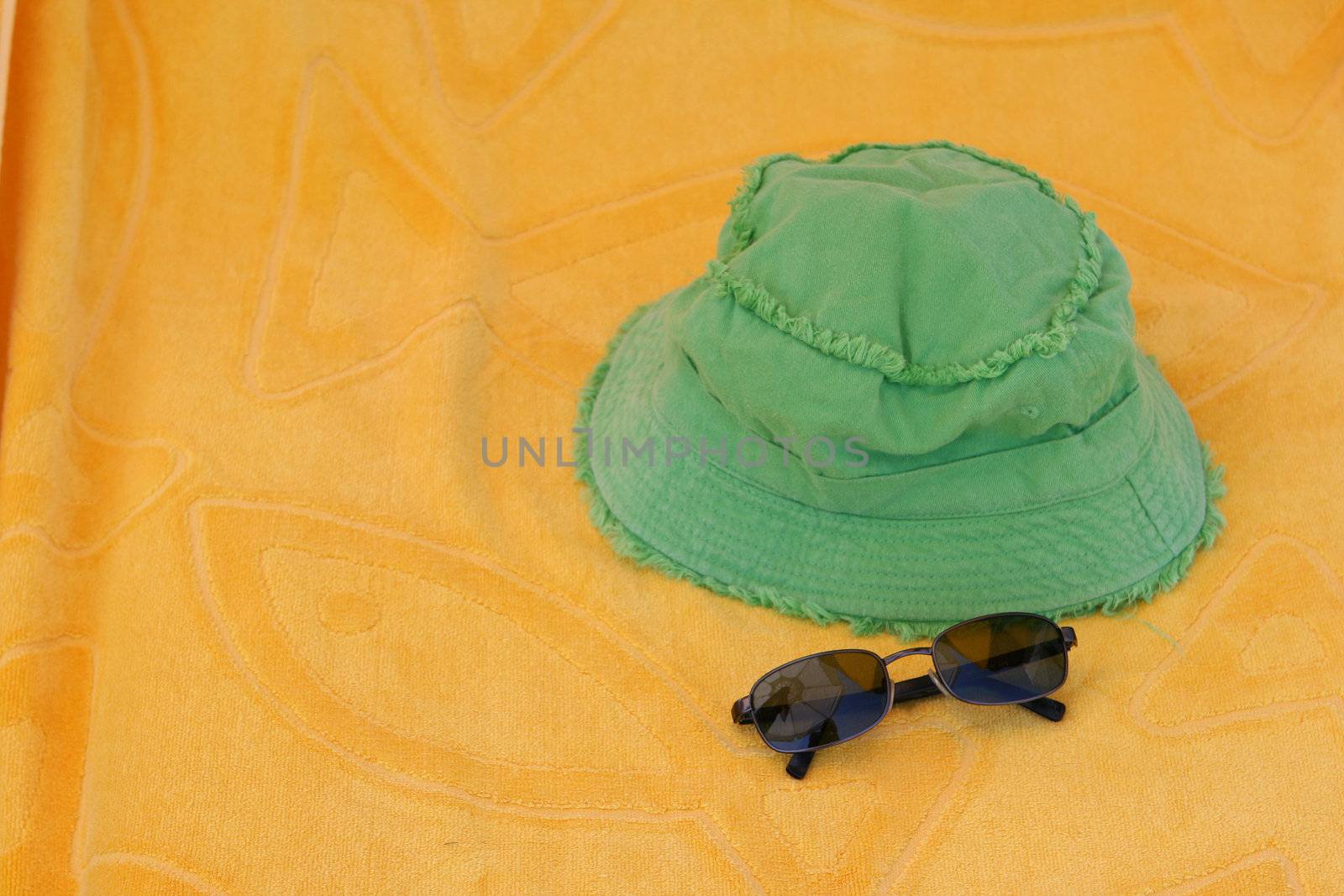 summer accessories green hat and black sunclasses on yellow towel