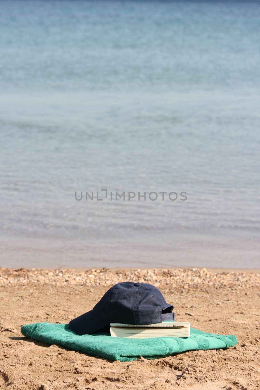 blue baseball hat on green towel by the see and book