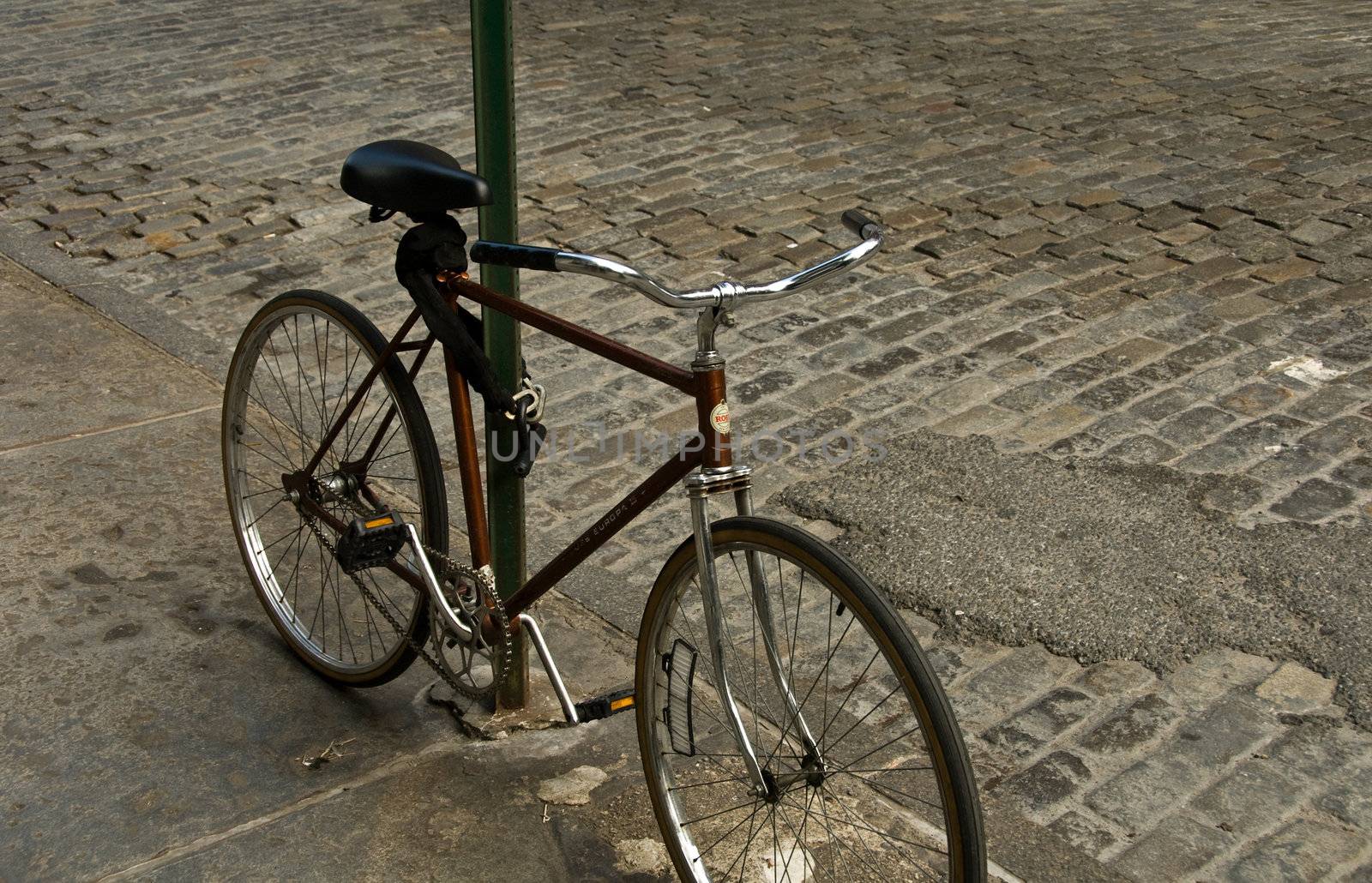 bicycle in nyc chained to post, brick road behind