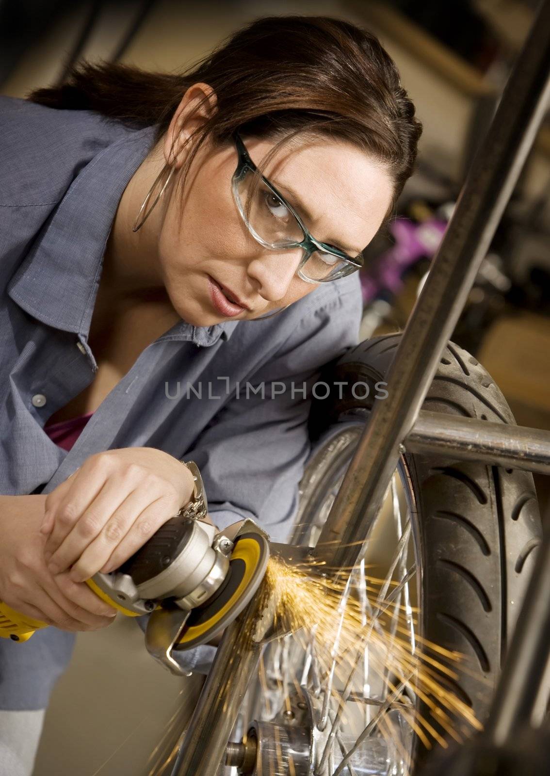 Hispanic woman using grinder tool on the front fork of motorcycle