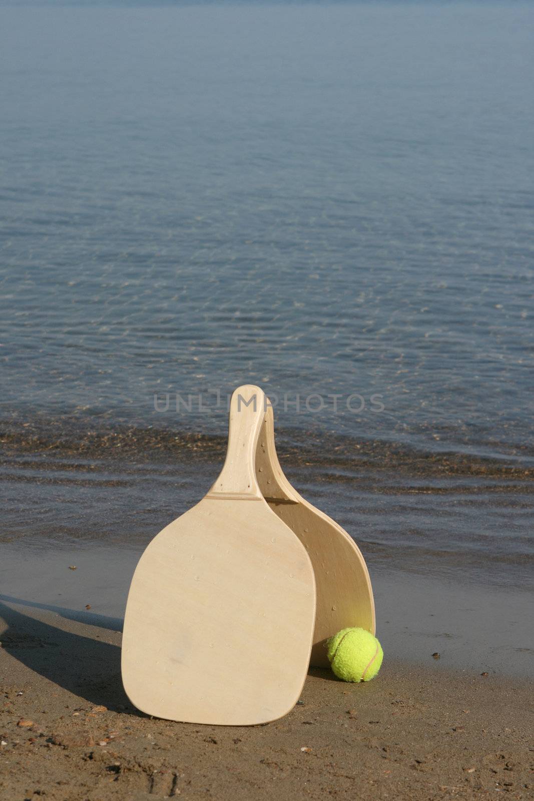 two wooden beach rackets by the shore with yellow ball