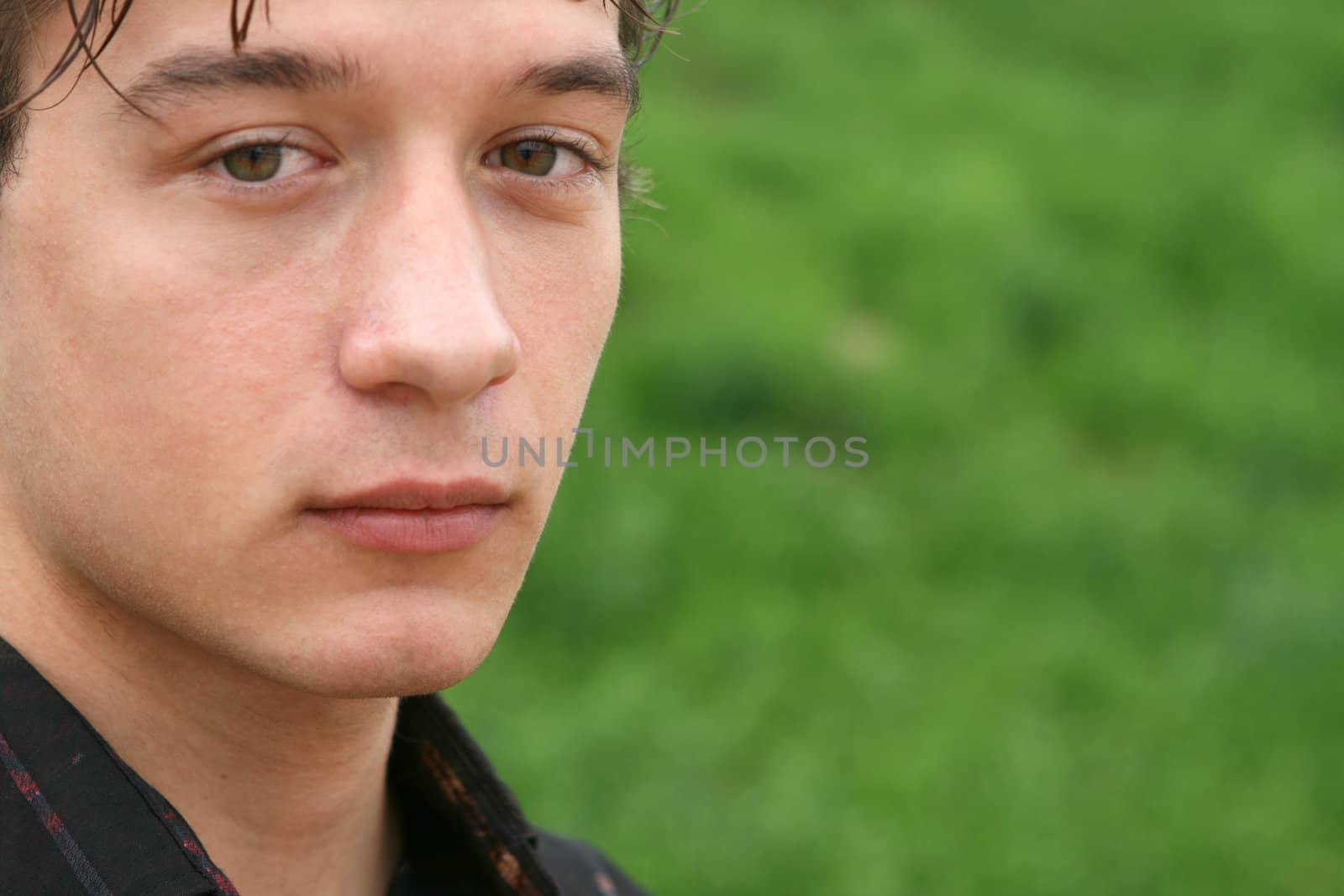closeup portrait of young man watcing the front seriously with blur green grass background for copy space