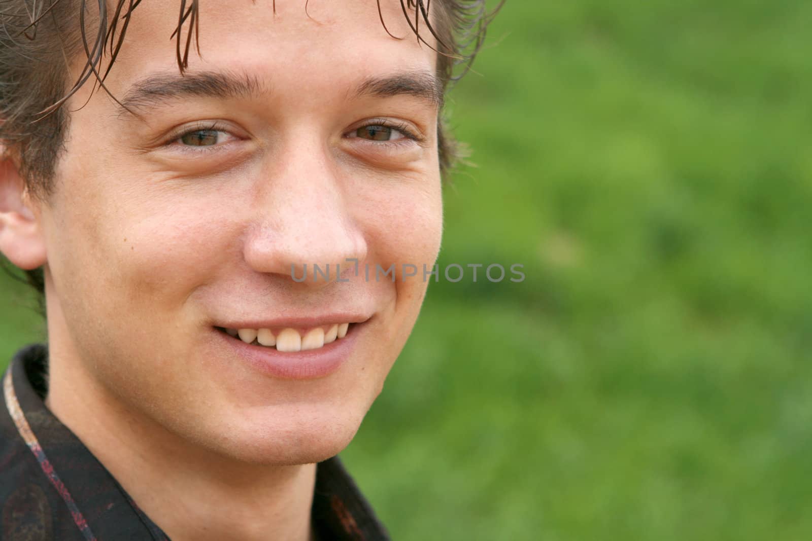 closeup portrait of young man watcing  front smiling with blur green grass background for copy space