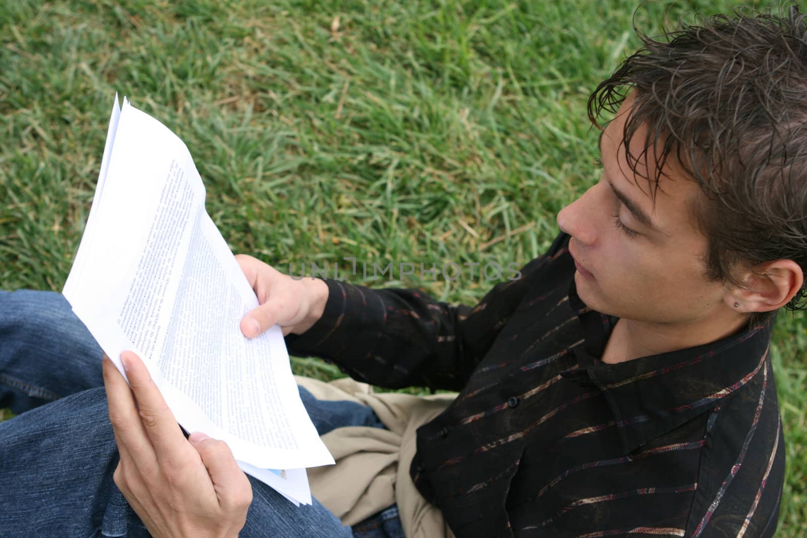 young student reading a document outdoors