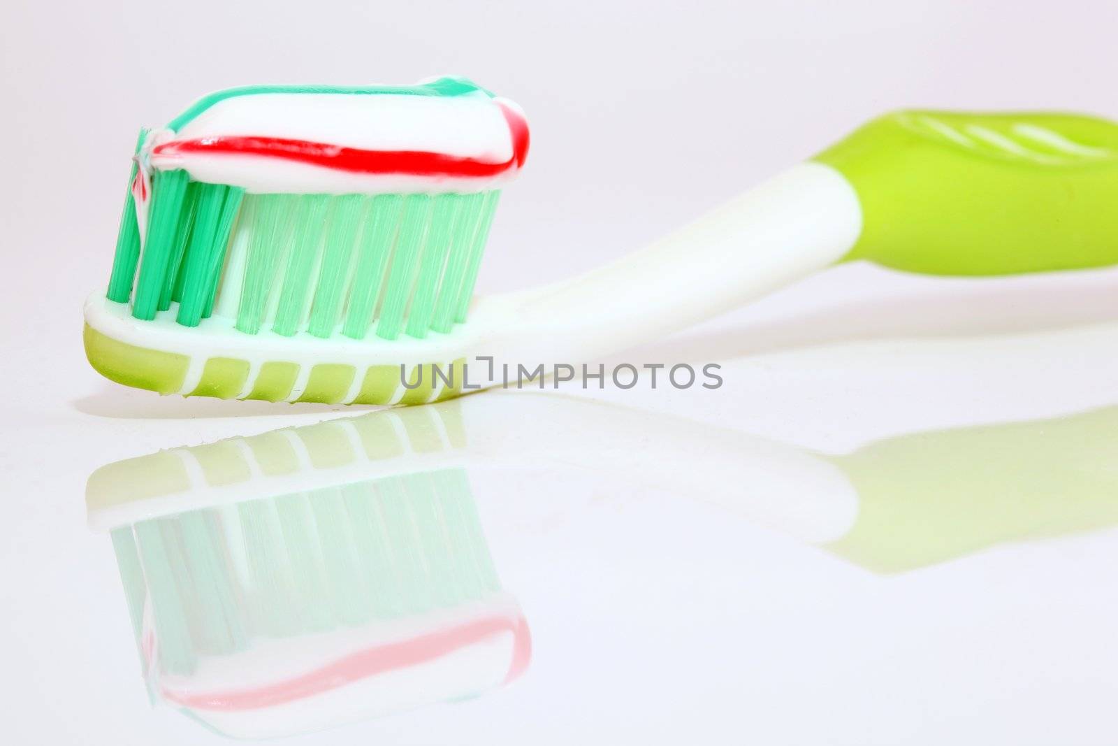 tooth paste on green brush closeup with beautiful reflection on white