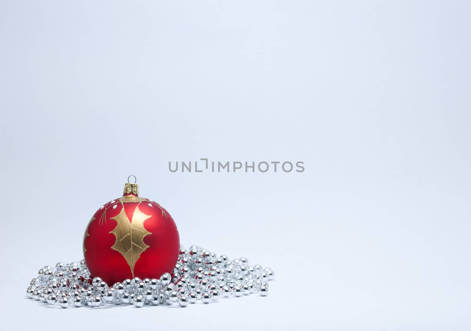 Single red and gold Christmas bauble with a gold holly leaf and silver beads on a white background.