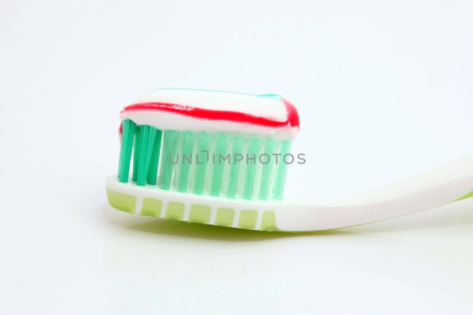 toothpaste on green toothbrush closeup on white background