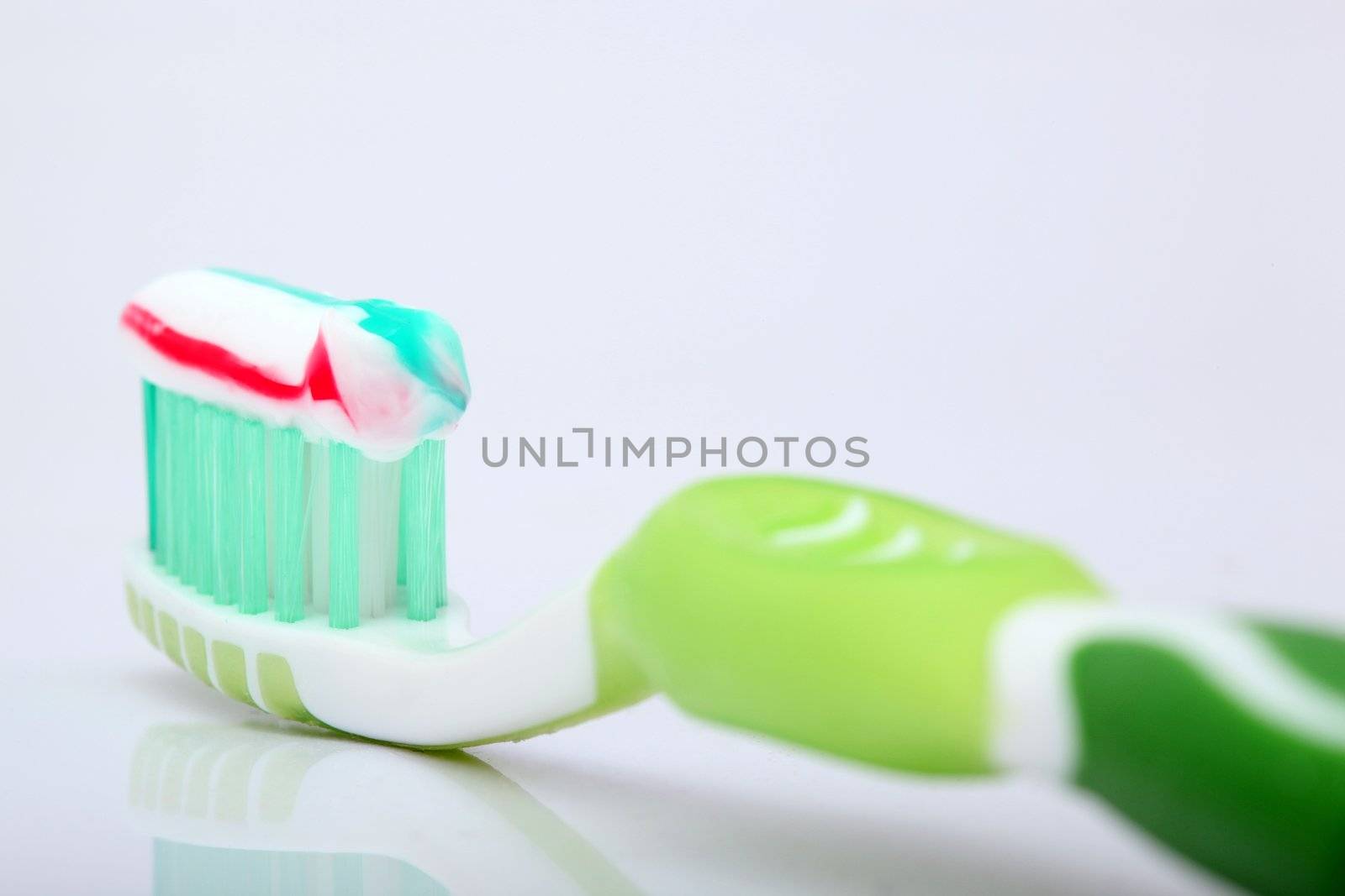 tooth paste on green brush closeup with beautiful reflection on white