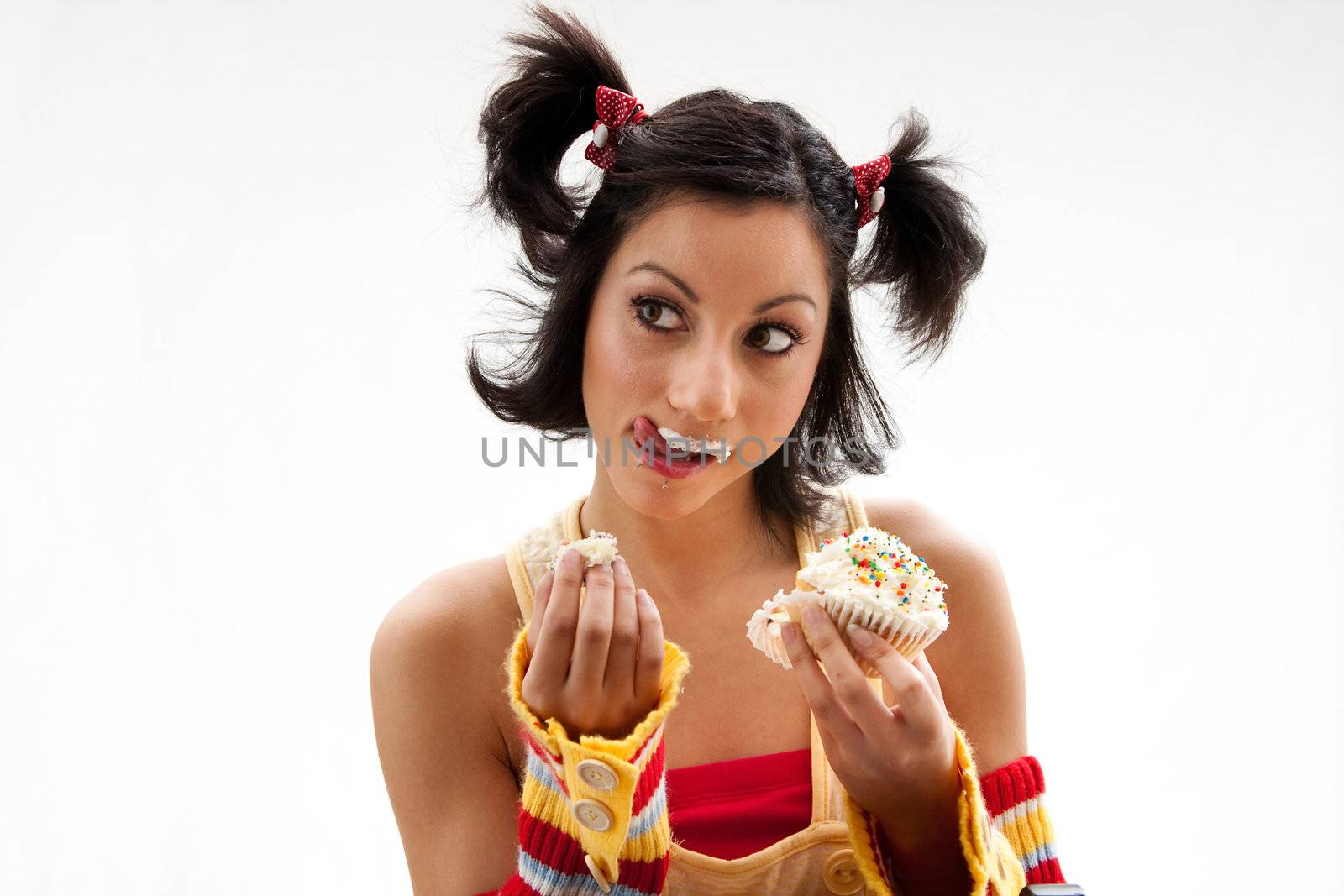 Beautiful Latina girl eating a cupcake with her fingers and licking her icing covered lip, isolated