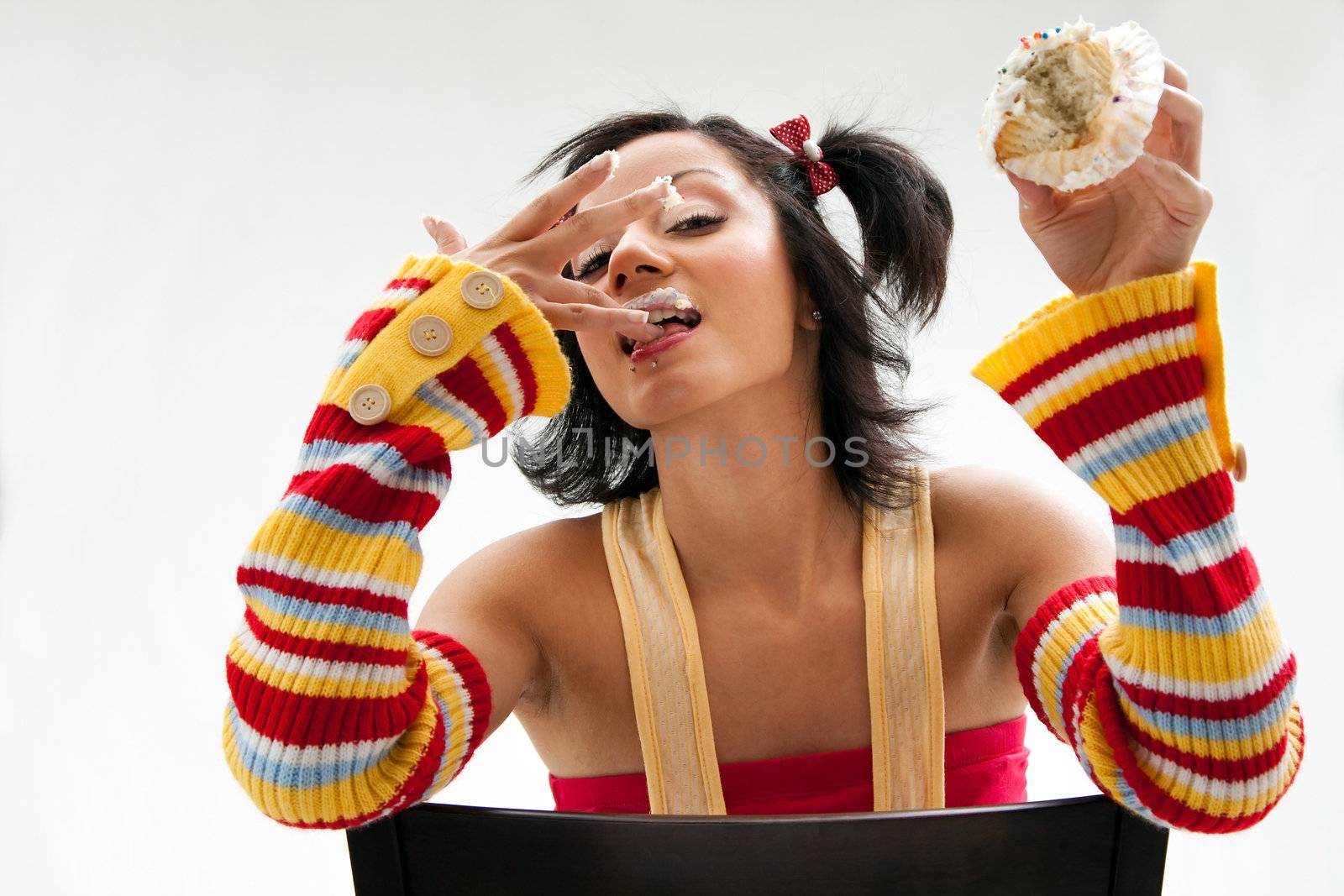 Beautiful Latina girl eating a cupcake licking her fingers and her icing covered lip, isolated