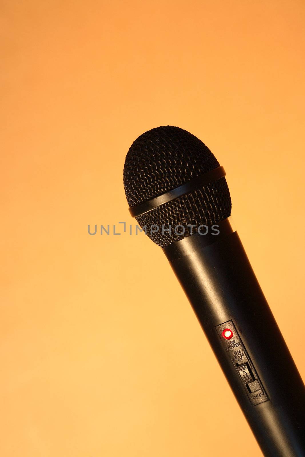 A modern black handheld ball head microphone on ginger background with copy space