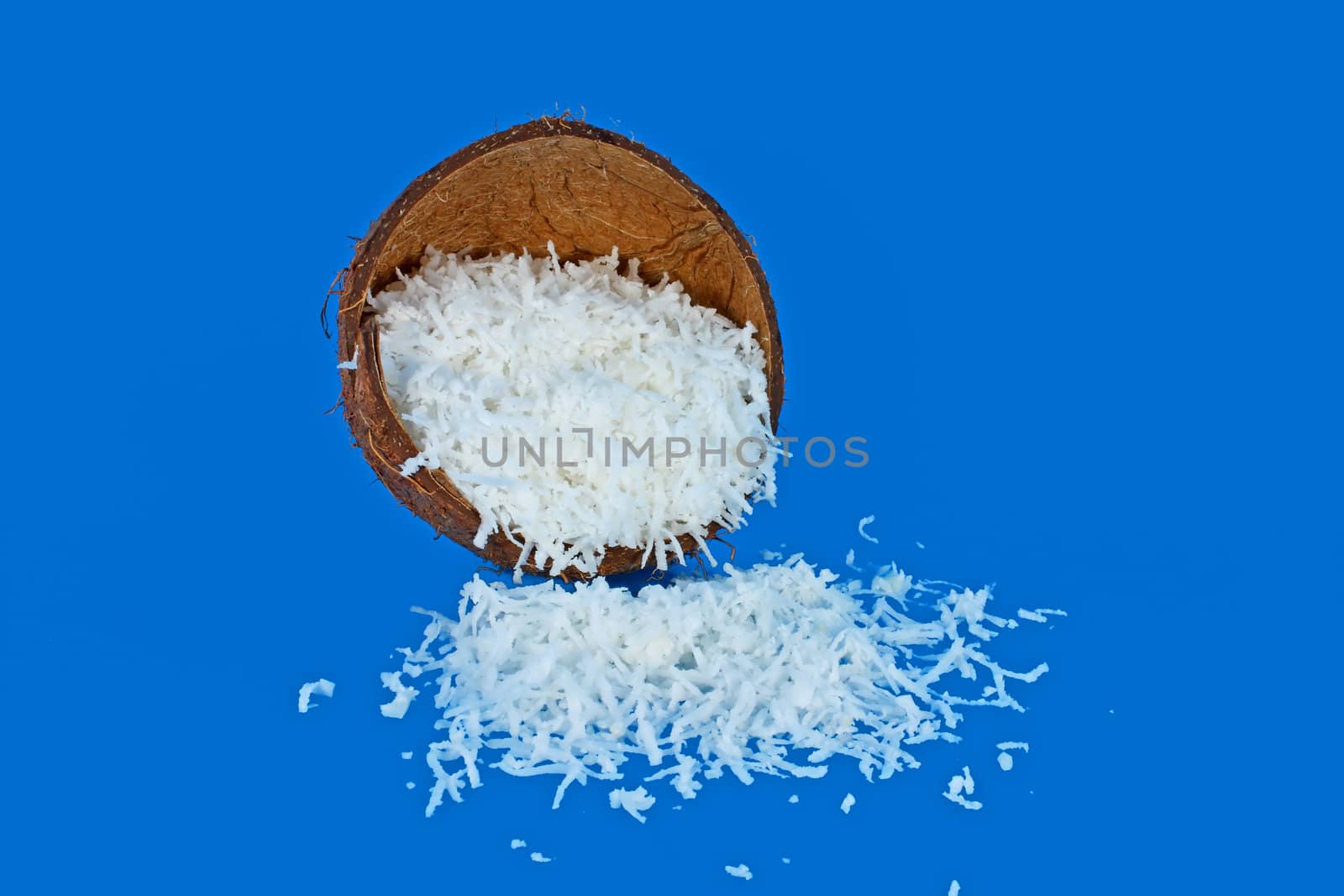 Half of coconut shell full of coconut meal isolated on blue