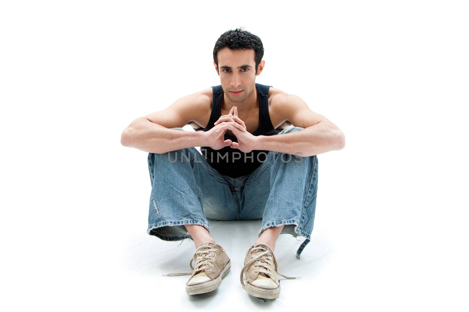 Handsome Caucasian guy wearing black tank top and jeans sitting on floor thinking, isolated