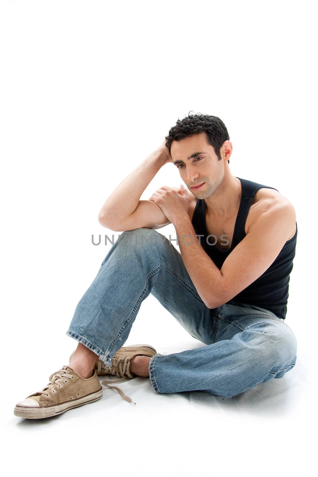 Handsome Caucasian guy wearing black tank top and jeans sitting on floor thinking, isolated