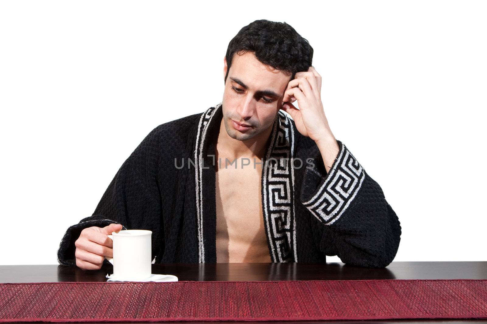 Handsome guy in the morning who just woke up sitting at a table in his robe with a cup, isolated on white