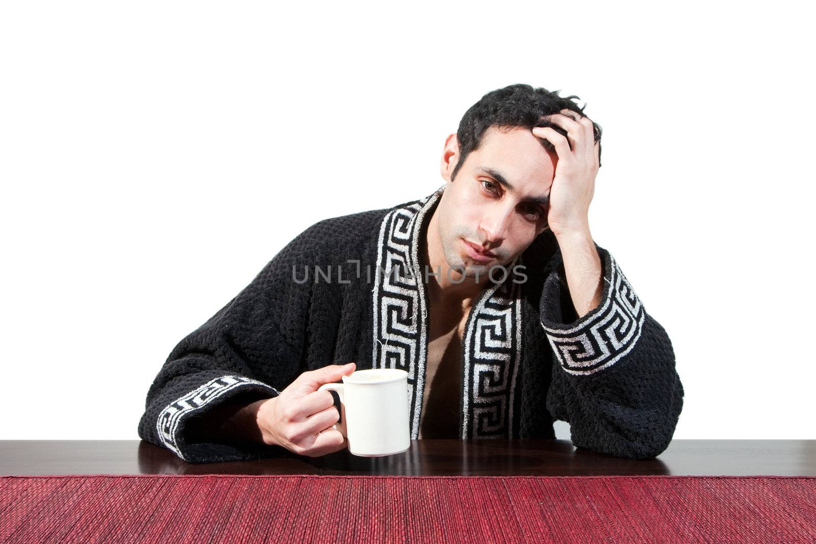 Handsome guy in the morning who just woke up sitting at a table in his robe with a cup recovering from his hangover, isolated on white