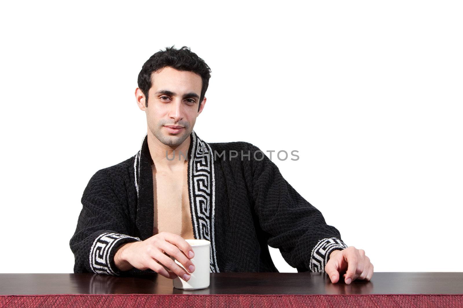 Handsome guy in the morning who just woke up sitting at a table in his robe with a cup, isolated on white