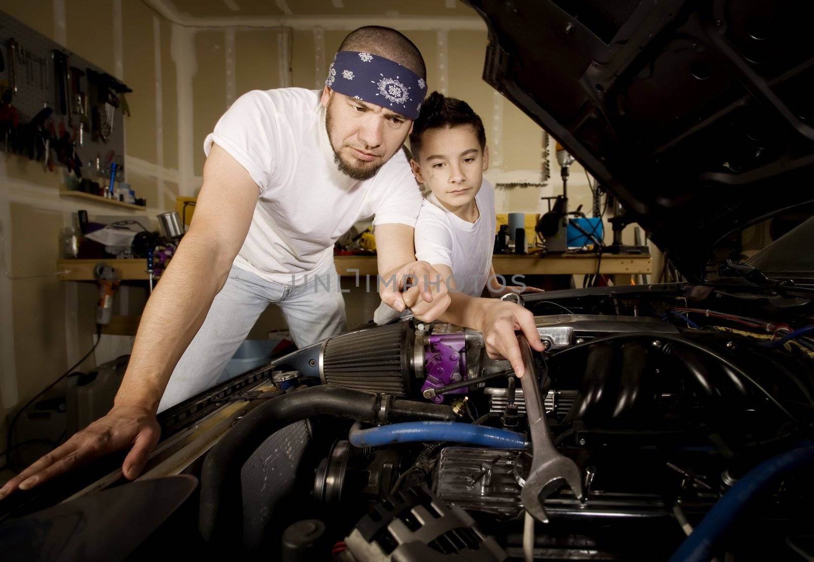 Hispanic father and son working on car engine in garage