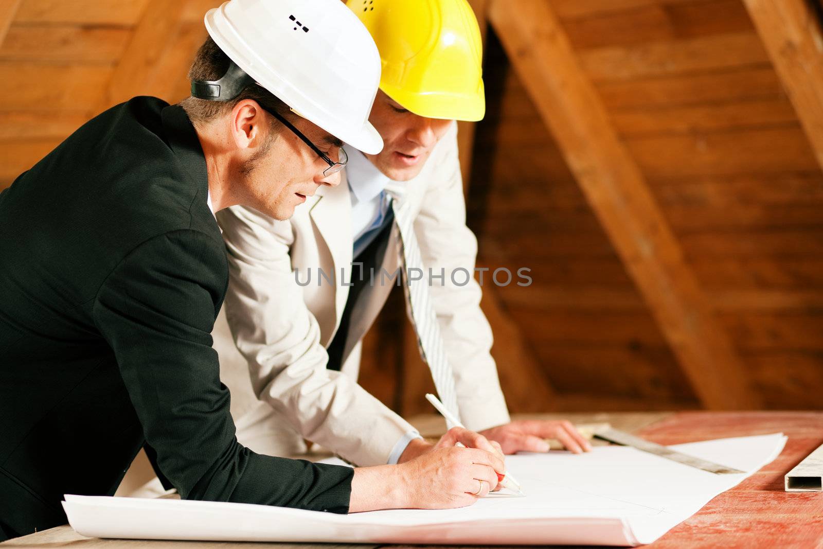 Architect and construction engineer or surveyor discussion plans and blueprints. Both are wearing hardhats and are standing on the construction site of a home indoors