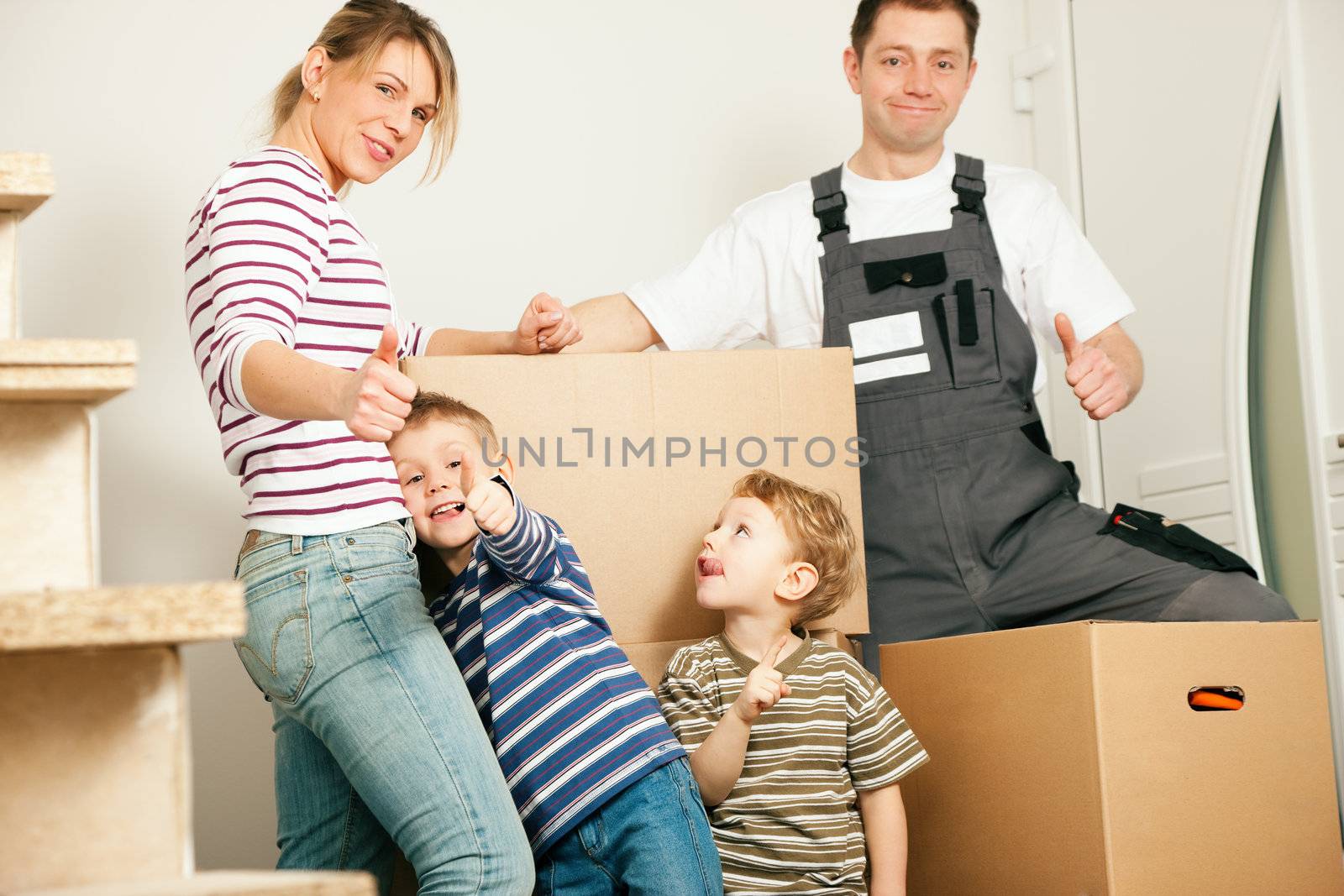 Family moving in their new house. They are standing in front of a stack of moving boxes being happy. Father is dressed in a way that can also represent a mover