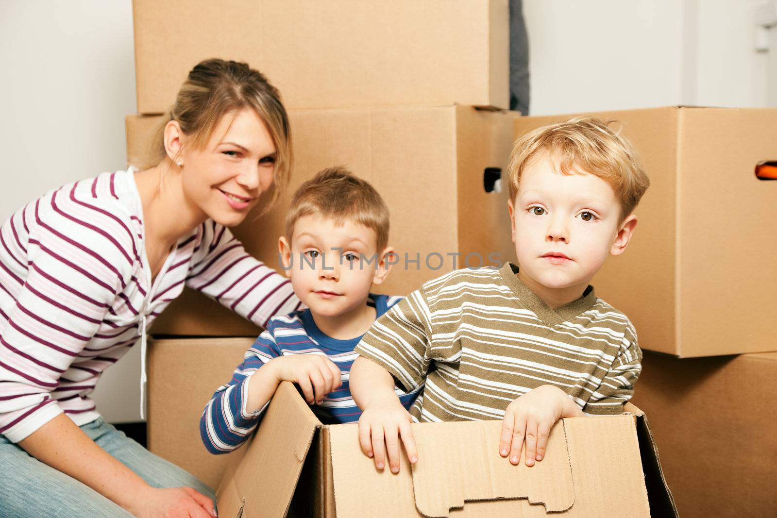 Family moving in their new house. The sons are sitting inside the moving boxes, everybody is looking rather cheerful