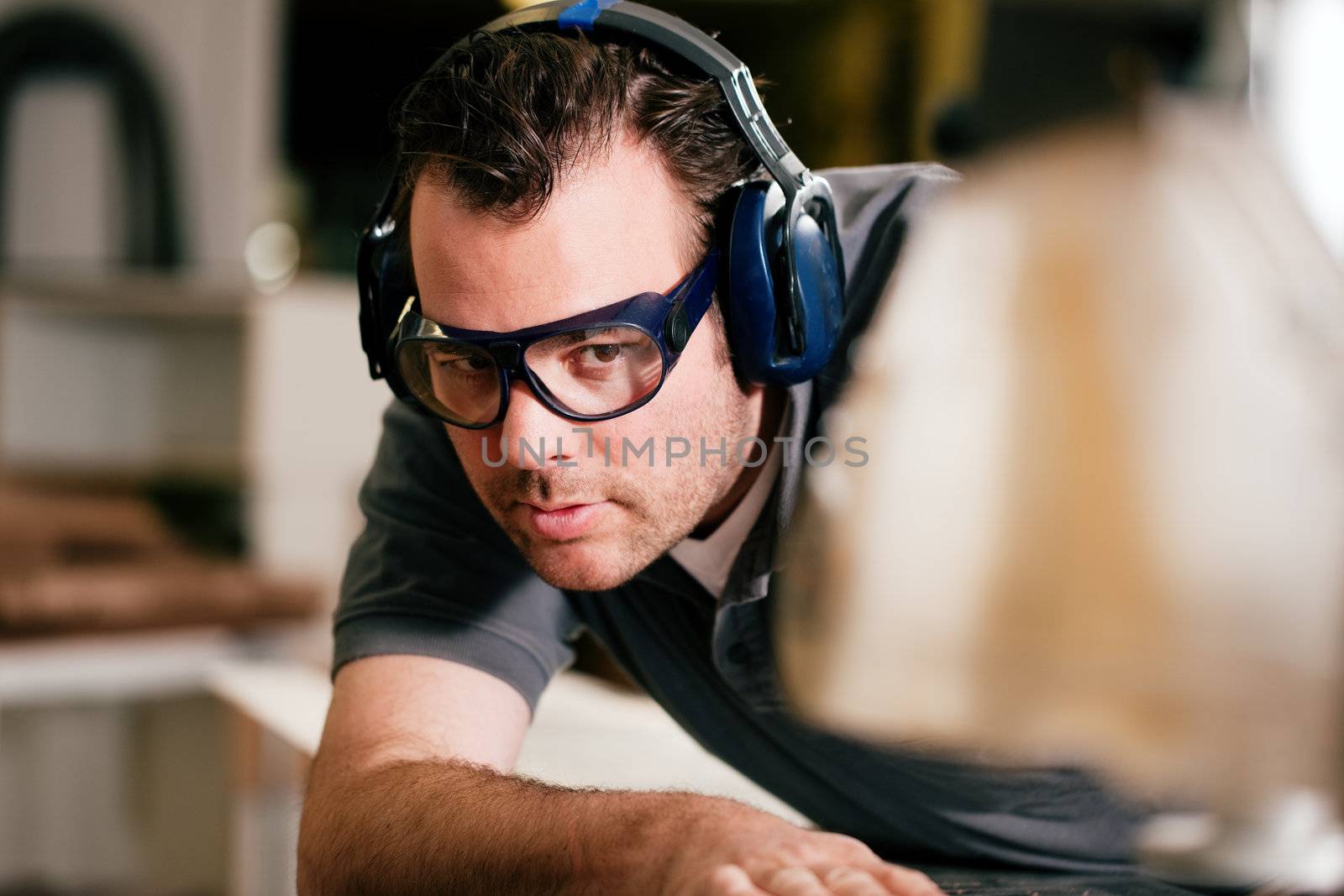 Carpenter working on an electric buzz saw cutting some boards, he is wearing safety glasses and hearing protection to make things safe