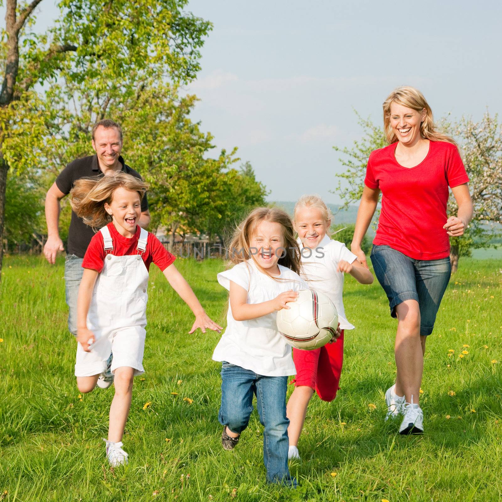 Happy family playing football, one child has grabbed the ball and is being chased by the others