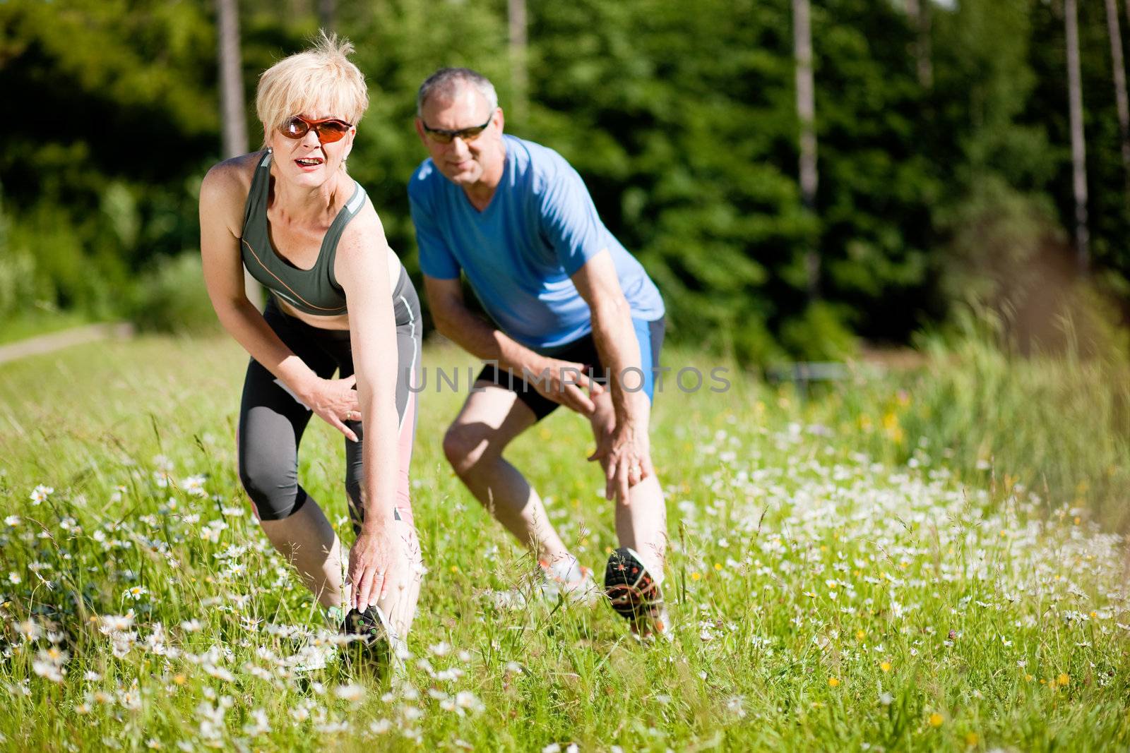 Mature or senior couple in jogging gear doing sport and physical exercise outdoors, stretching and gymnastics