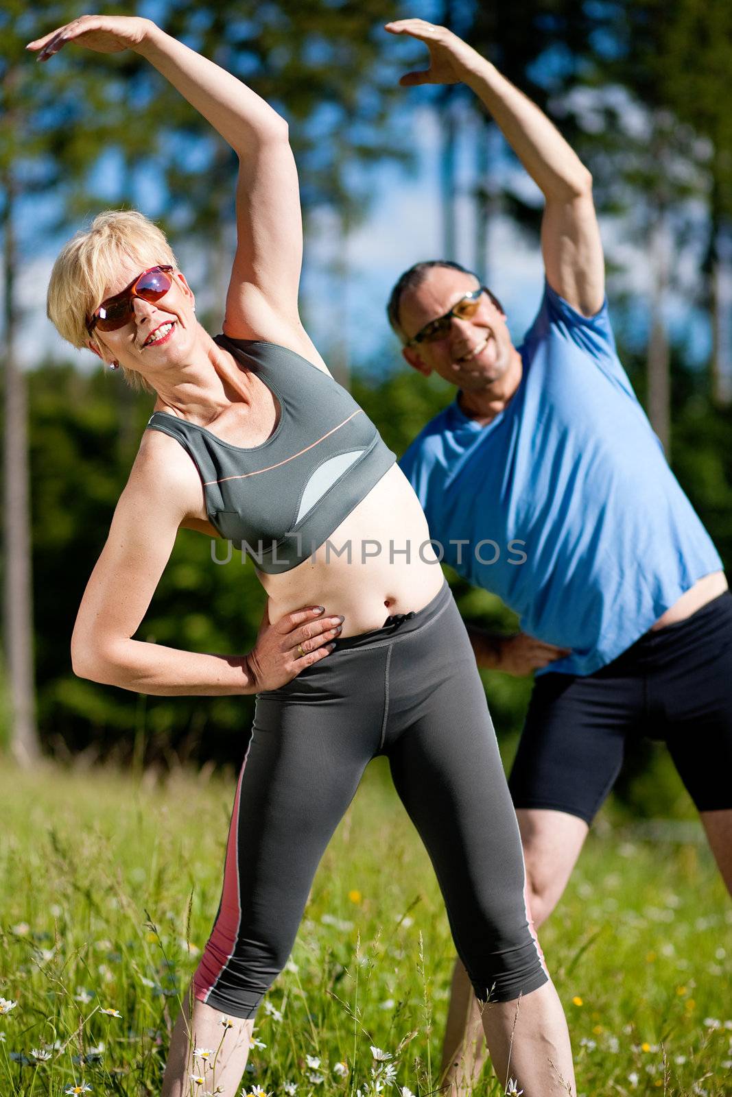 Mature or senior couple in jogging gear doing sport and physical exercise outdoors, stretching and gymnastics