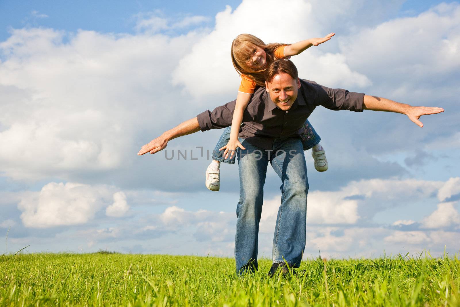 Father and his kid - daughter - playing together at a meadow, he is carrying her piggyback