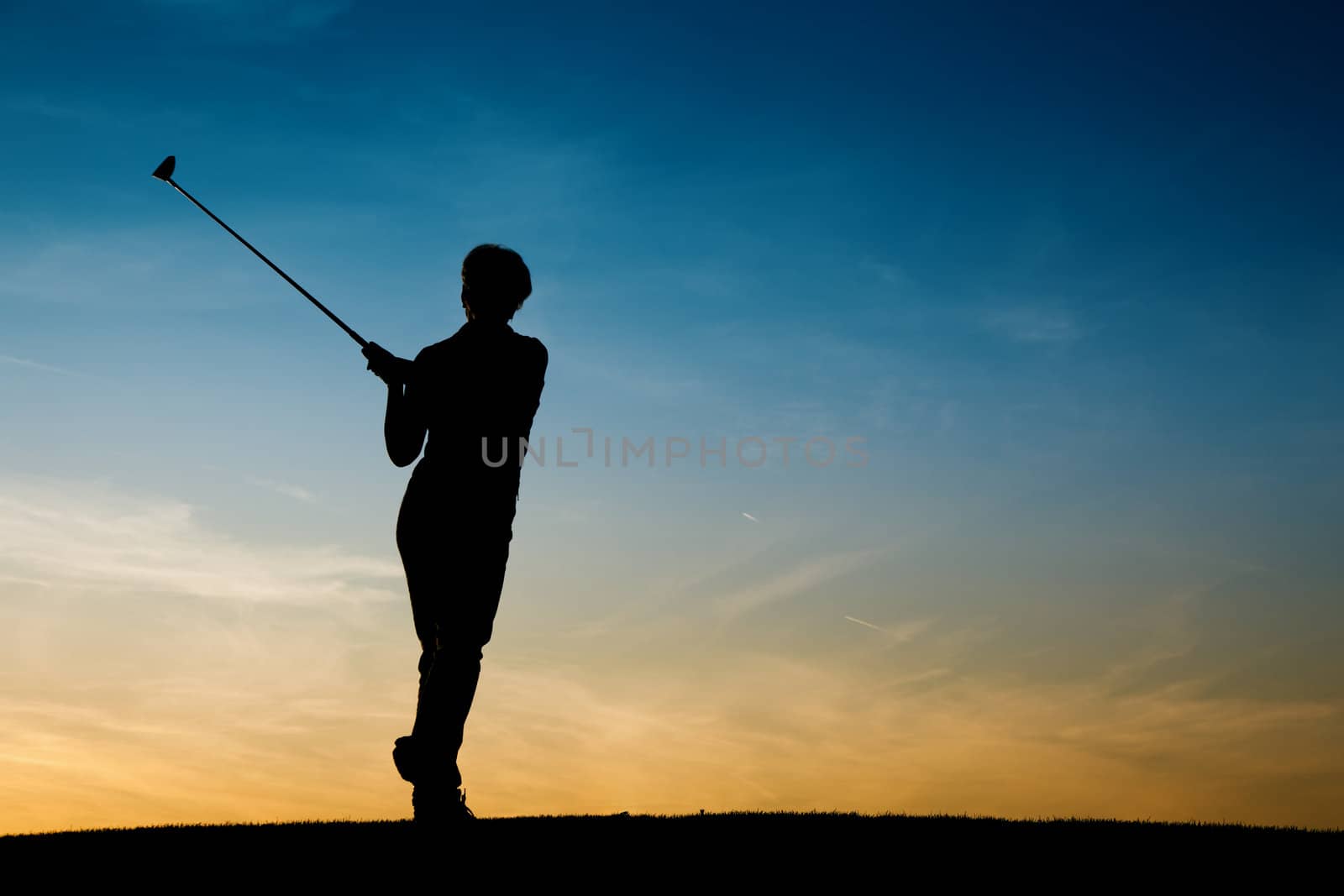 Senior woman playing golf - pictured as a silhouette against an evening sky