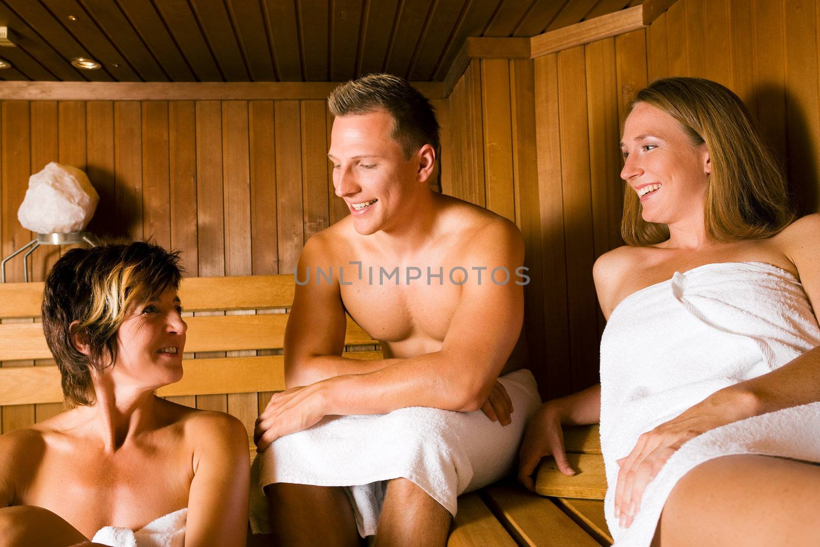 Three people (one male, two female) enjoying a hot sauna, talking to each other