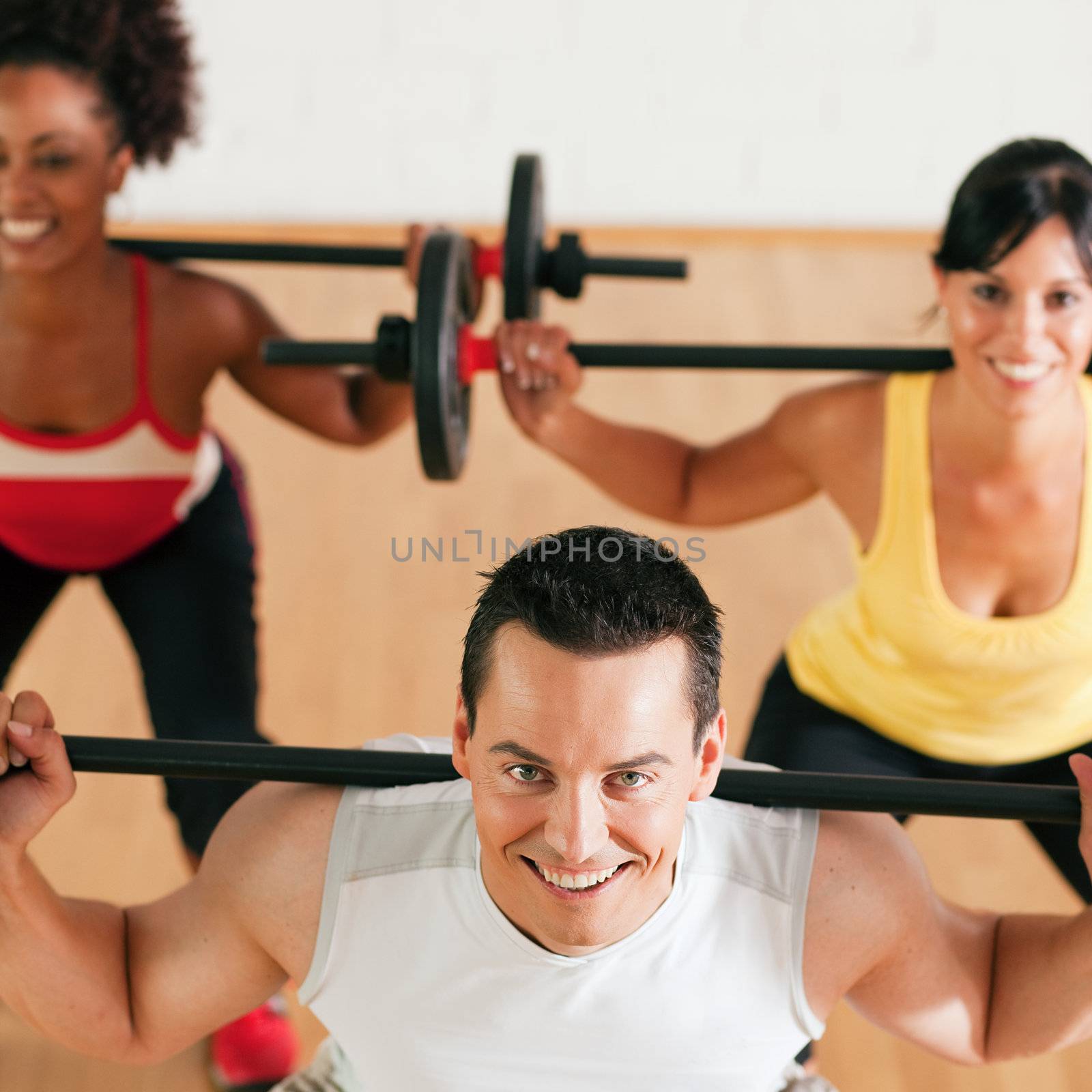 Group of three people exercising using barbells in the gym to gain strength and fitness