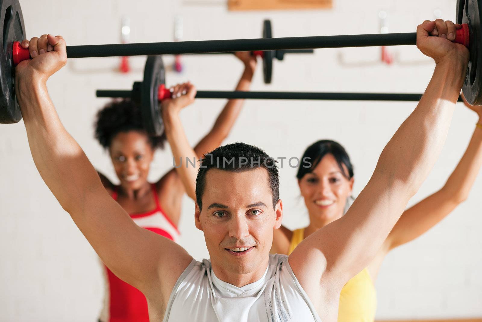 Group of three people exercising using barbells in the gym to gain strength and fitness