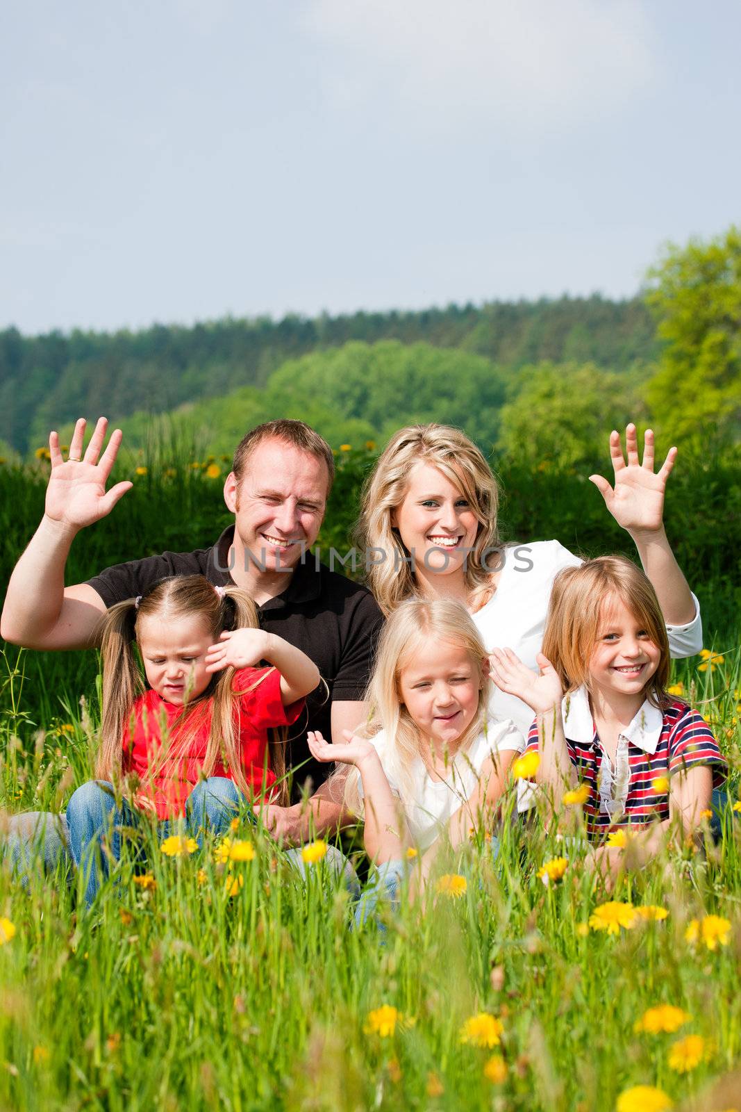 Happy family sitting in a meadow full of dandelions in spring, waving