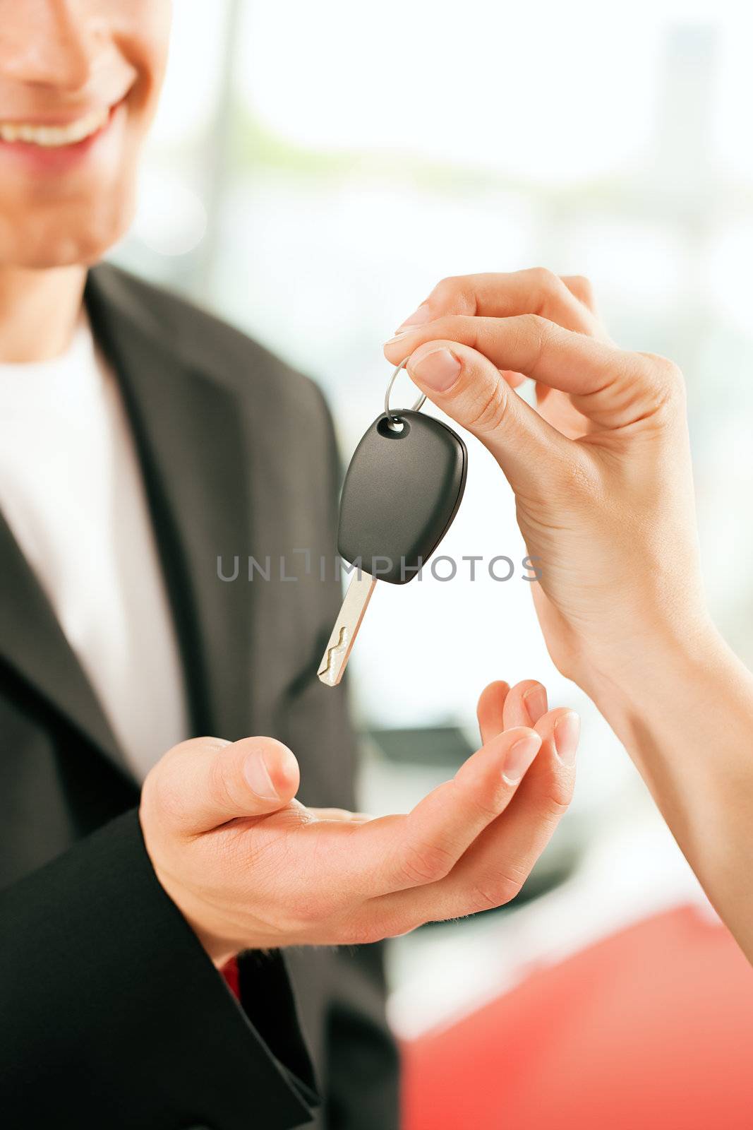 Man at a car dealership buying an auto, the female sales rep giving him the key, macro shot with focus on hands and key
