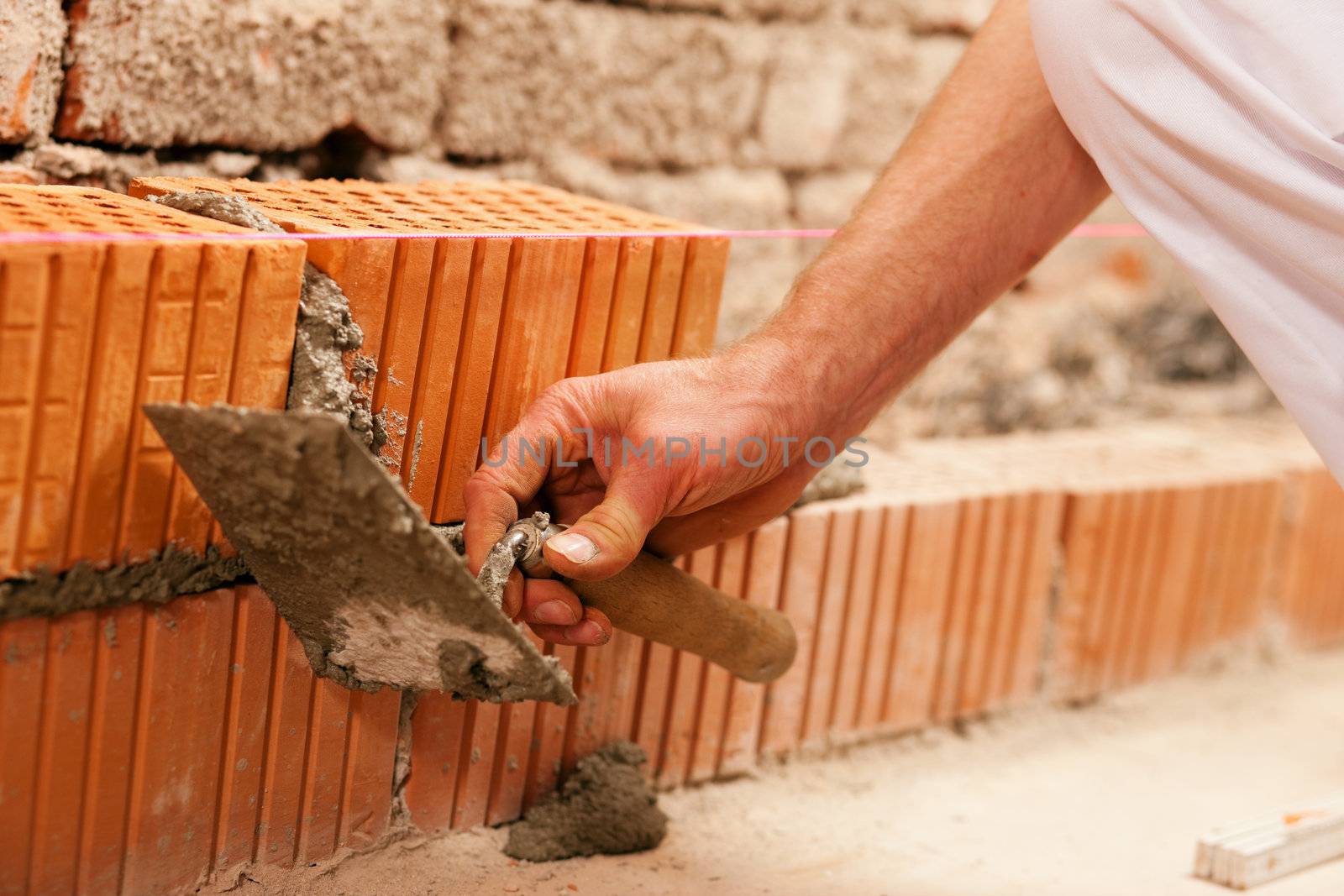bricklayer laying, well, bricks to make a wall, he is putting grout on a brick with his trowel. This man is really working hard