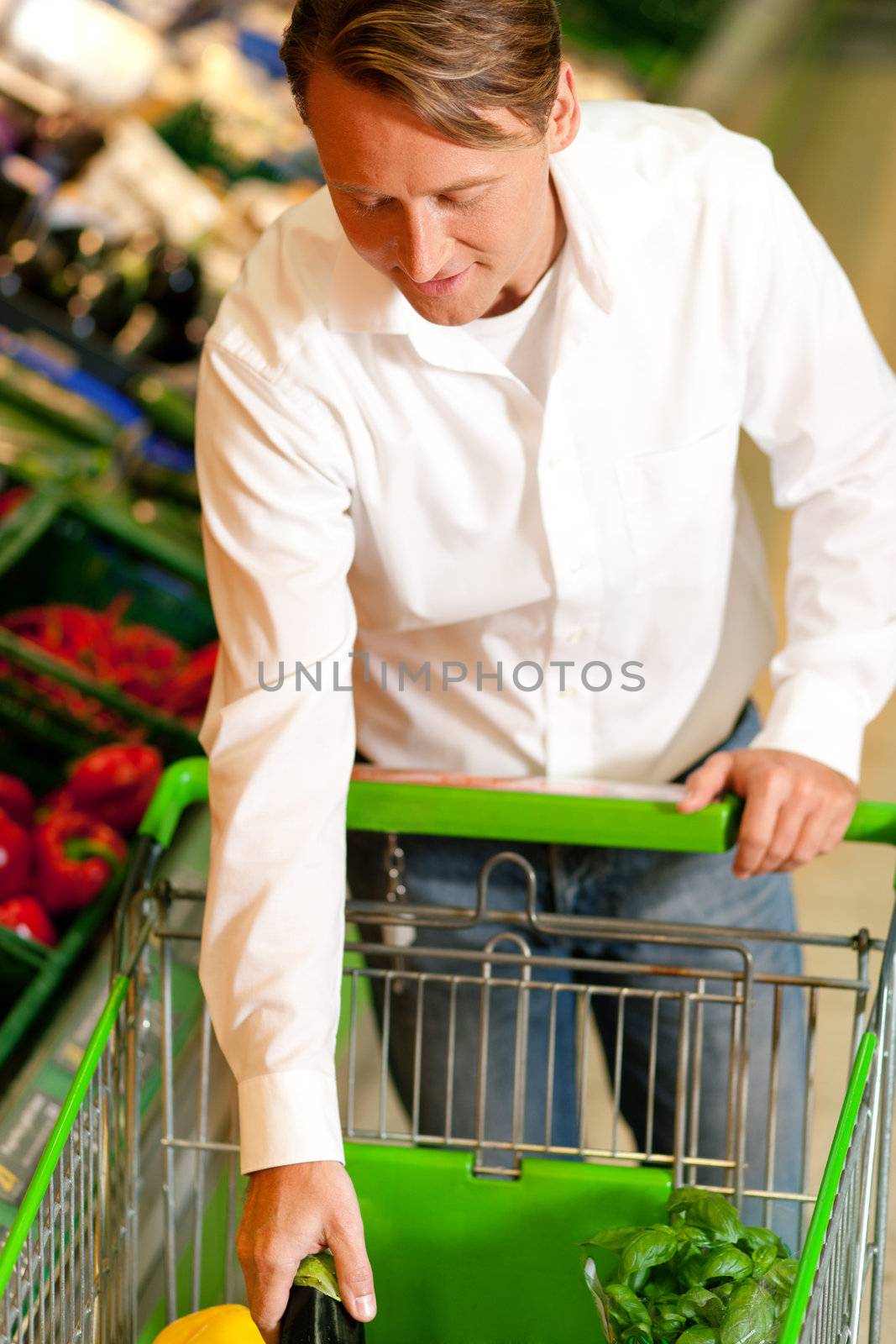 Man in a supermarket at the vegetable shelf shopping for groceries, he is putting some stuff into the shopping cart