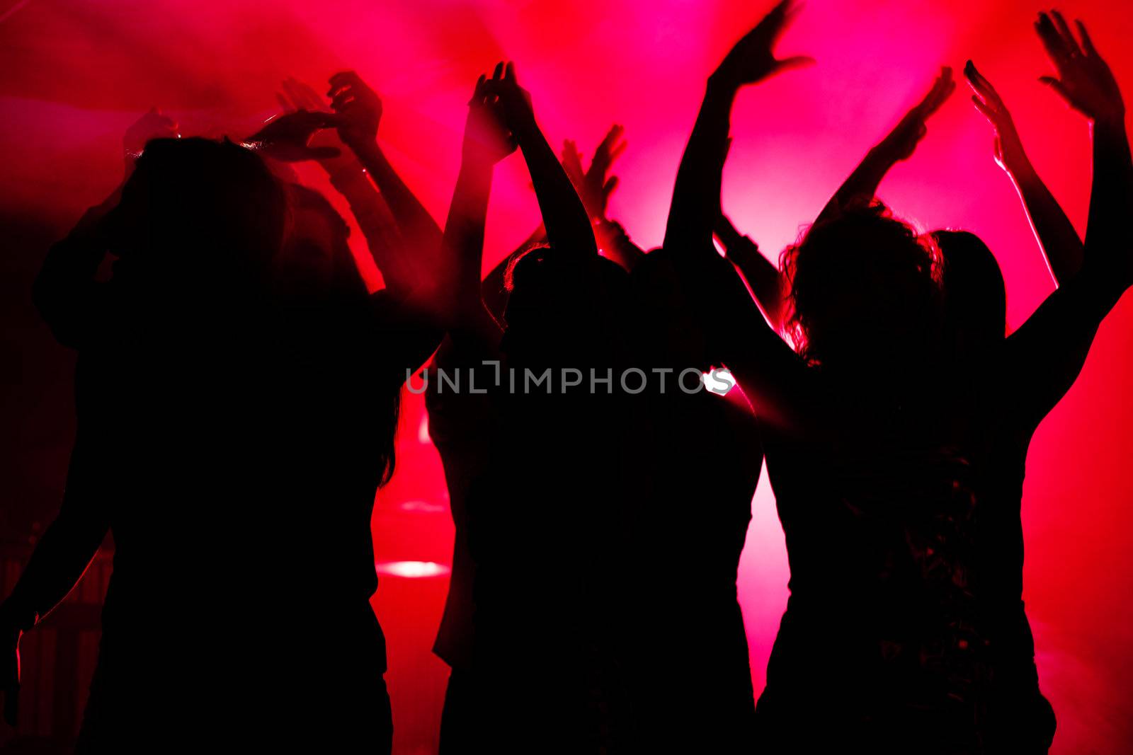 Silhouettes of dancing people having a celebration in a disco club, light is shining through the silhouettes of people