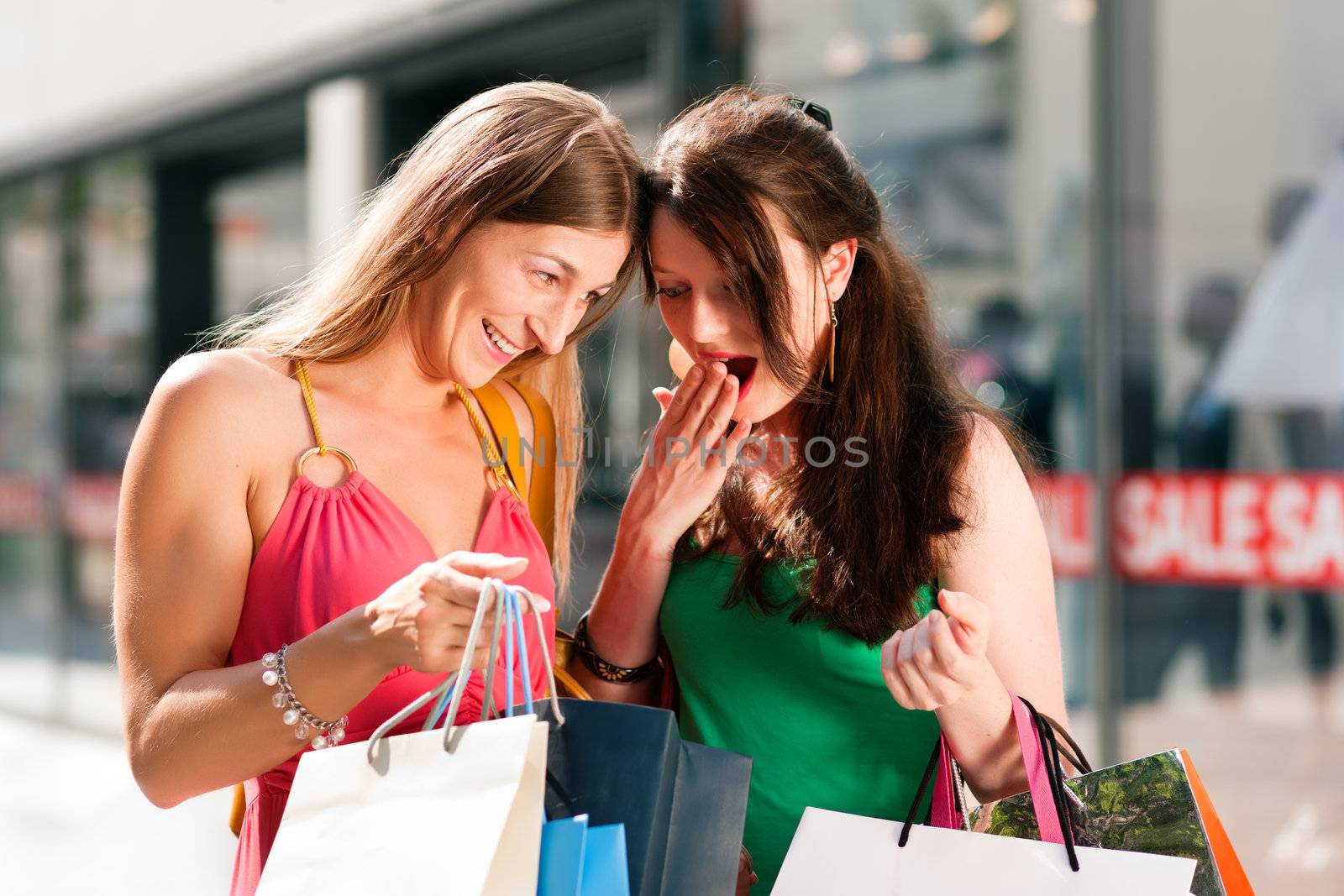 Two women being friends shopping downtown with colorful shopping bags, in the background a store can be seen with the words "sale" in the window