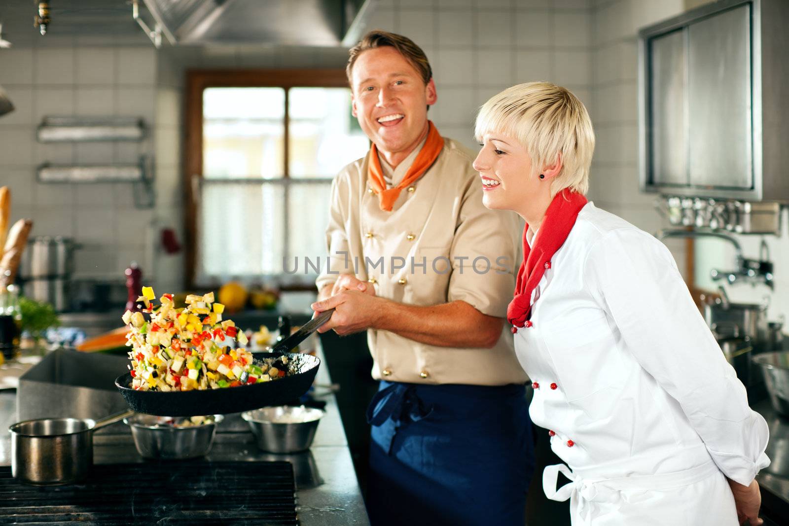 Two chefs in teamwork - man and woman - in a restaurant or hotel kitchen cooking delicious food, he is working on the ratatoulle in the pan