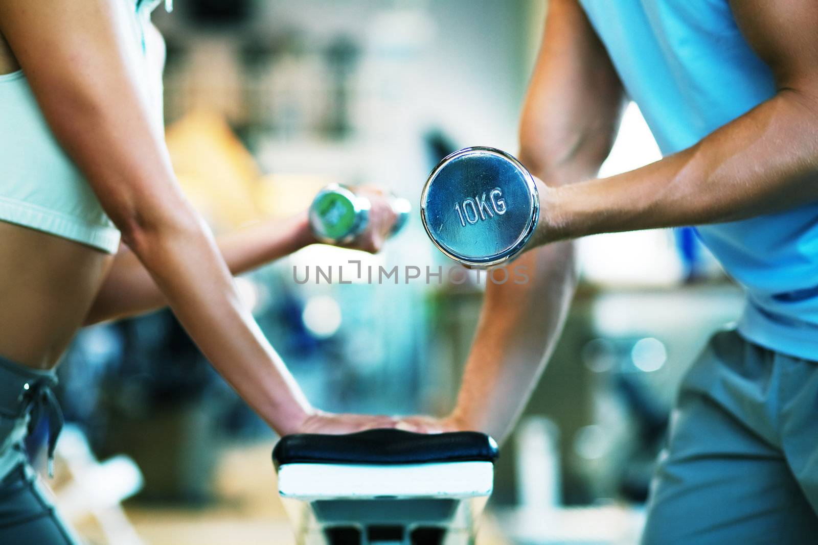 A man and a woman (only arms and body) lifting dumbbells (focus on dumbbell, shallow depth of field)