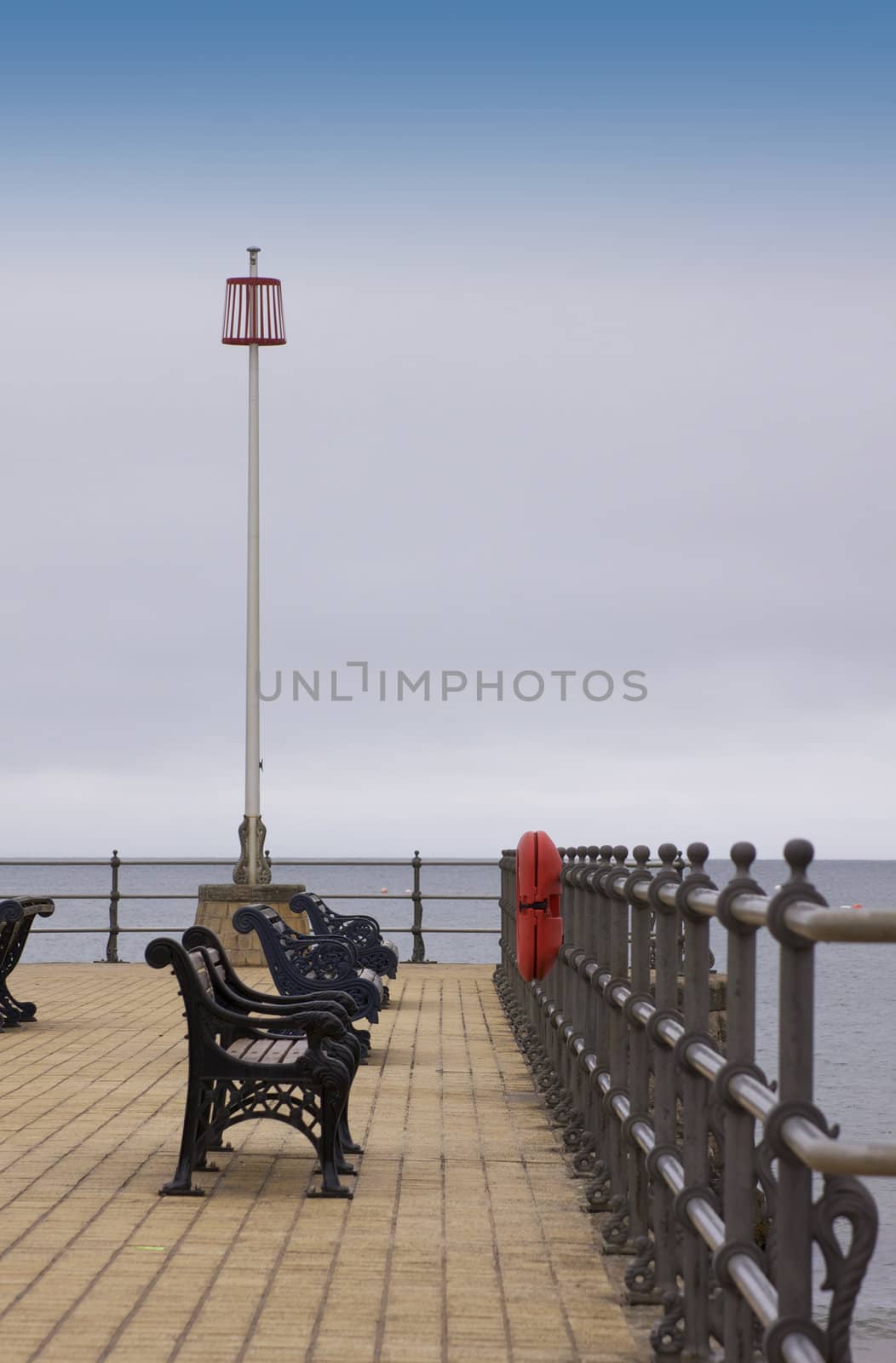 The view of the end of a pier. located at Swanage beach, Swanage in Dorset. Iron benches are set on a brick paved platform with steel railings.